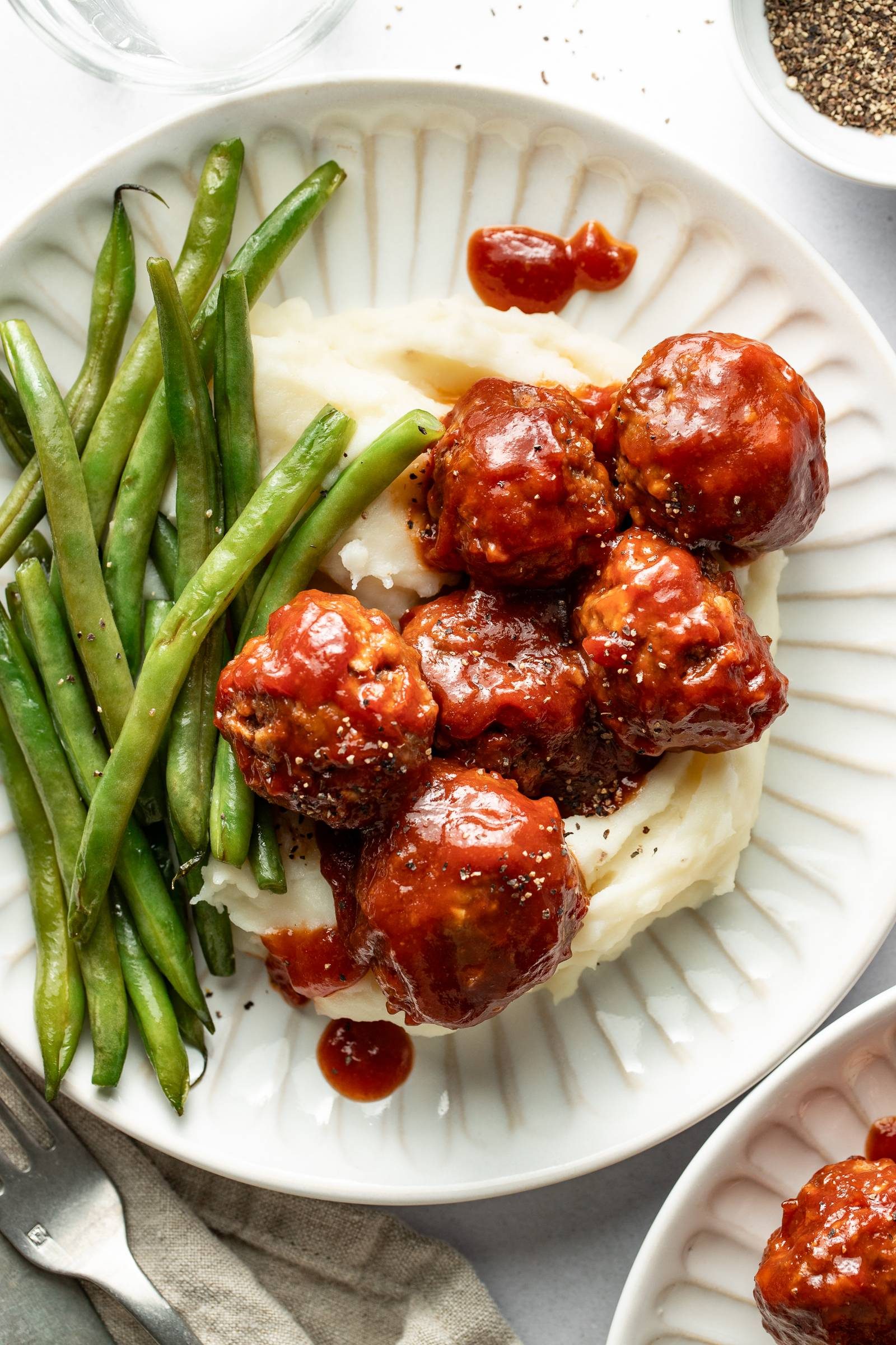 BBQ meatballs on a plate with mashed potatoes and green beans.